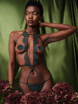 An open playsuit in forest green featuring delicate lace and silk straps, featuring an open design for the breasts and the bum, shown on model with matching nipple covers that are available in shop only.