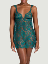 Teal lace slip with a sheer floral pattern, V neckline, delicate straps, and a scalloped lace hem, worn on a model.