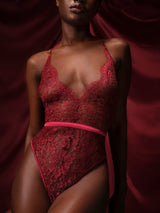 A red lurex Leaver's lace playsuit with a halterneck shape, delicate eyelash trim at the bust, and a silk band at the waist. It includes sleek adjustable silk straps and delicate golden hardware. Shown on model