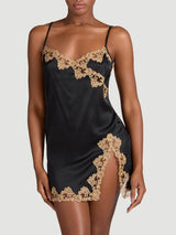 Model showing the front of a Coco de Mer black silk slip dress. The slip has an embroidered gold trim along the hem and bust, a v-neckline and leg slit.