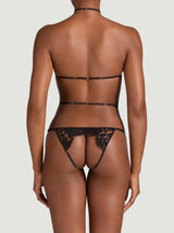 The back view of a model wearing the Aphrodite open playsuit. Made from a black, sheer French Leavers lace paired with adjustable silk strapping for the perfect fit. This is an open style with silk and lace framing the body.