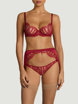A model wearing an intricate red French Leaver's lace and luxurious silk suspender knicker with a high waist and adjustable straps, featuring golden hardware and scallop edge lace details.