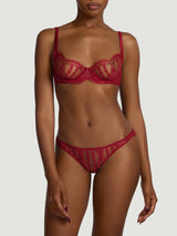 A model wearing a red plunge bra made from a delicate French leaver's lace and silk. Scallop edges run across the neckline edge of the cups and at the under band. It is finished with red silk wire casing, adjustable straps and a hook and eye closure.
