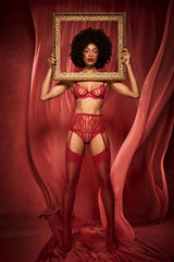 A model wearing a red French Leavers lace suspender belt featuring a scalloped edge along the bottom and a red silk waistband at the top. There are two suspender clips at both the front and the back in the centre of each leg. This is paired with a delicate Brazillian knicker made from a red floral French leaver's lace and scallop edge details. Alongside is a red plunge bra made from a delicate French leaver's lace and silk. Scallop edges run across the neckline edge of the cups and at the under band.