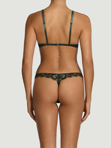 Model showing the back of a dark green lingerie set from Coco de Mer. Featuring dark floral embroidery on a sheer tulle throughout. Scalloped edges along the the thong back and silk covered bra straps in a matching forest green. 