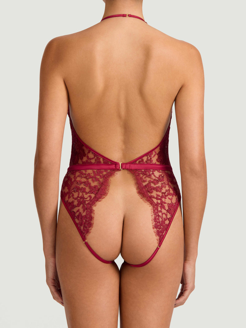 A red lurex Leaver's lace playsuit with a halterneck shape, delicate eyelash trim at the bust, and a silk band at the waist. It includes an open bottom, sleek adjustable silk straps and delicate golden hardware.