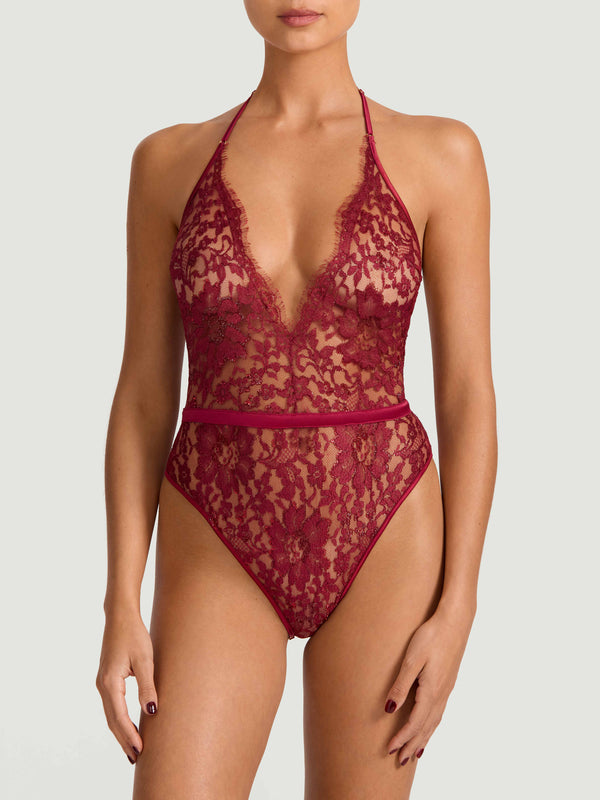 A red lurex Leaver's lace playsuit with a halterneck shape, delicate eyelash trim at the bust, and a silk band at the waist. It includes sleek adjustable silk straps and delicate golden hardware. Shown on model