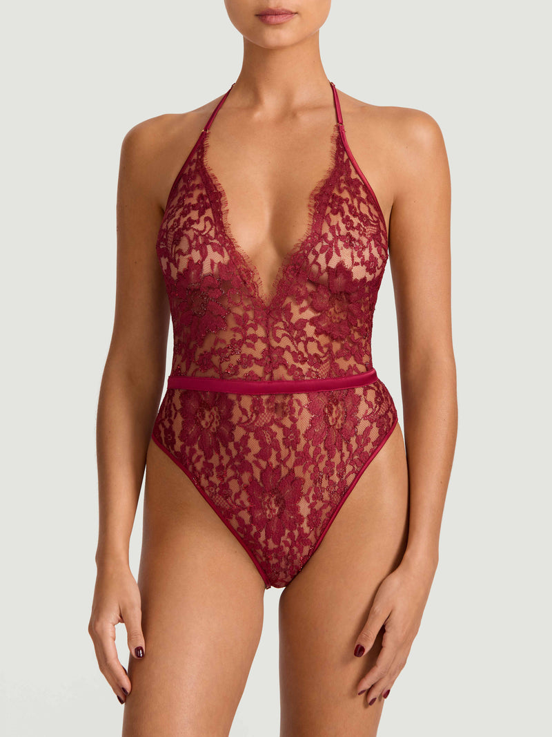 A red lurex Leaver's lace playsuit with a halterneck shape, delicate eyelash trim at the bust, and a silk band at the waist. It includes sleek adjustable silk straps and delicate golden hardware. Shown on model