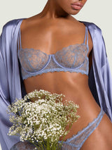 Model wearing a powder blue Coco de Mer floral embroidered bra and thong set, holding a bridal bouquet, with a matching silk robe. 