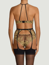 Model wears the black suspender belt in a UK size S/M with rose design gold embroidery scallop edge detailing attached to black sheer hold ups by black silk straps paired with matching brazilian knickers and black underwire plunge bra with gold embroidery in a UK size 34B