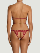 Back view of a model wearing an intricate red French leavers lace open playsuit. Featuring red silk binding straps, scallop edge lace panels framing the bottom and an open crotch.
