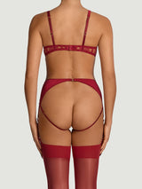 A model wearing an intricate red French Leaver's lace and luxurious silk suspender knicker with a high waist and adjustable straps, featuring golden hardware and scallop edge lace details. This is paired with a red quarter cup bra featuring details of scallop edged Leaver's Lace lining a silk covered quarter cup and silk straps with a hook and eye closure at the spine.