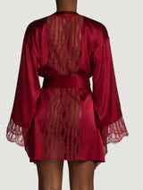 The back view of a model wearing the Coco de Mer Renata robe. This is a red silk robe featuring a panel of red French leaver's lace down the centre back and along the bottom cuffs of the sleeve. There is a red silk tie that creates a flattering shape at the waist when tied.