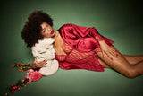A model wearing a short red slip made from a delicate red French leaver's lace with a plunging neckline and side split at the bottom right leg. The neckline and hemline feature a scalloped edge lace detail. There is a red silk under band and shoulder straps.