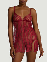A model wearing a short red slip made from a delicate red French leaver's lace with a plunging neckline and side split at the bottom right leg. The neckline and hemline feature a scalloped edge lace detail. There is a red silk under band and shoulder straps.